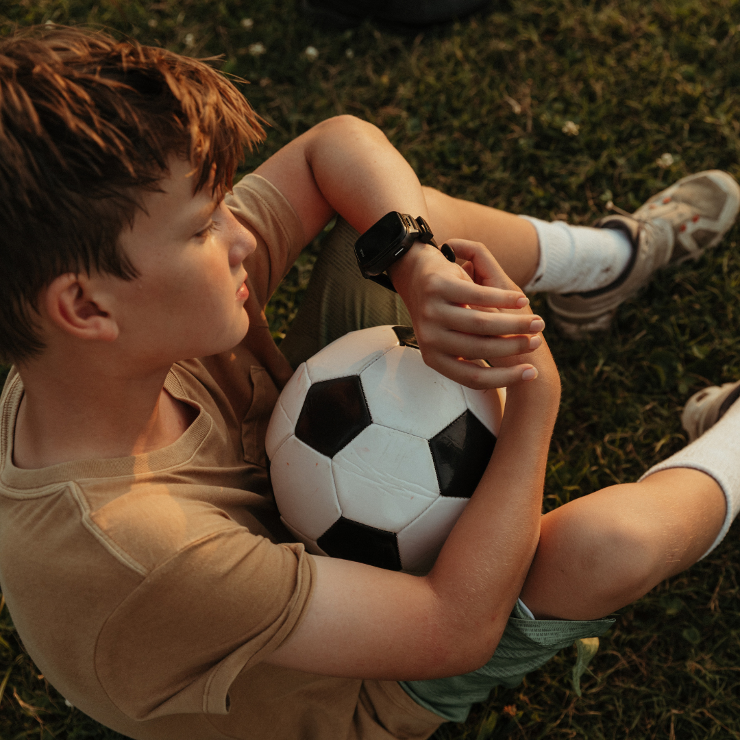 Child sitting on grass holding a soccer ball using Cosmo JrTrack 5
