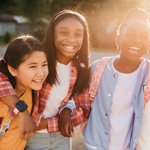 Three young girls smiling outdoors with a warm, sunlit background
