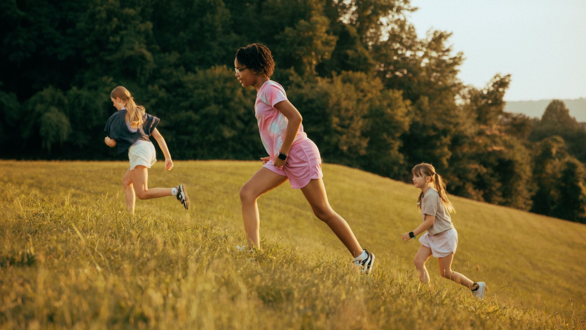 Three girls running up a hillside at sunset